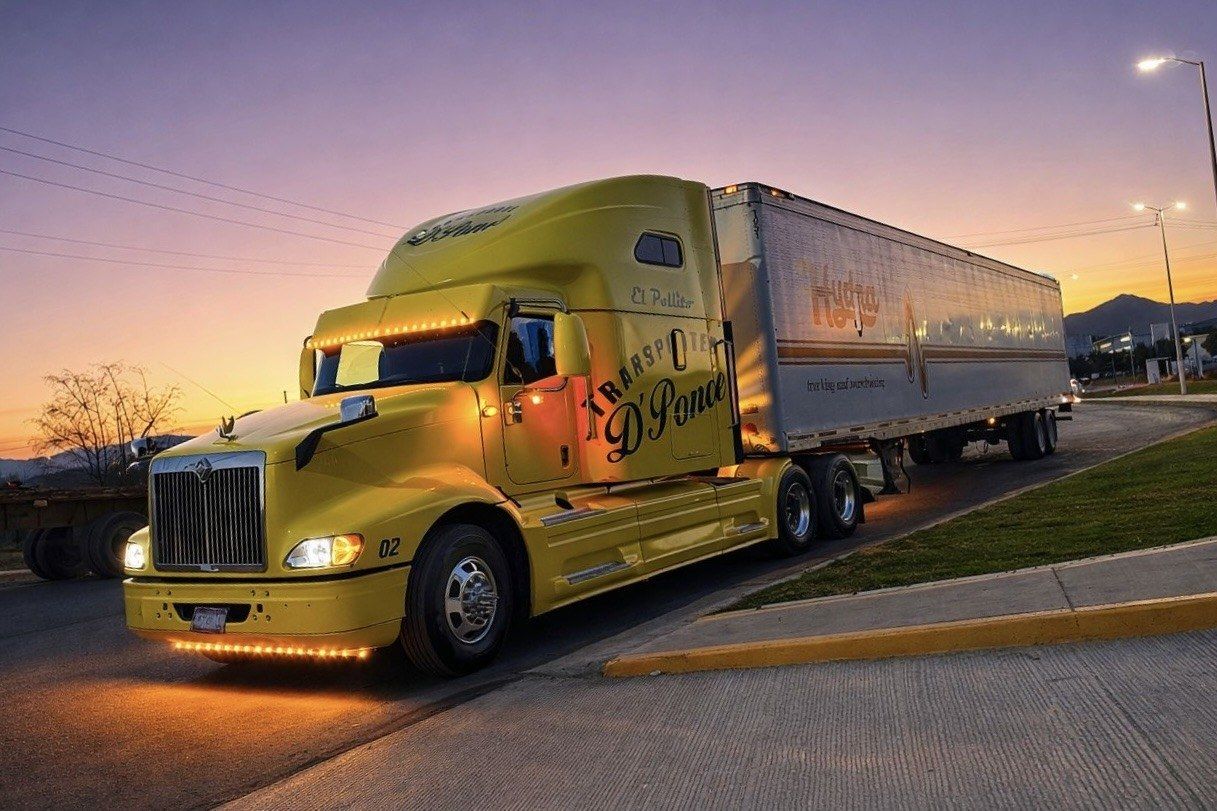 Tractocamión amarillo de Transportes D Ponce con caja, al atardecer