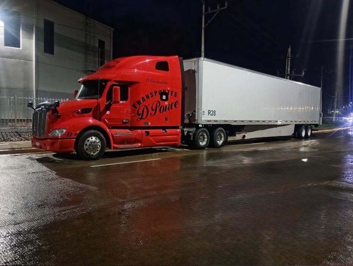 Tractocamión rojo de Transportes D Ponce con caja seca, cargando de noche